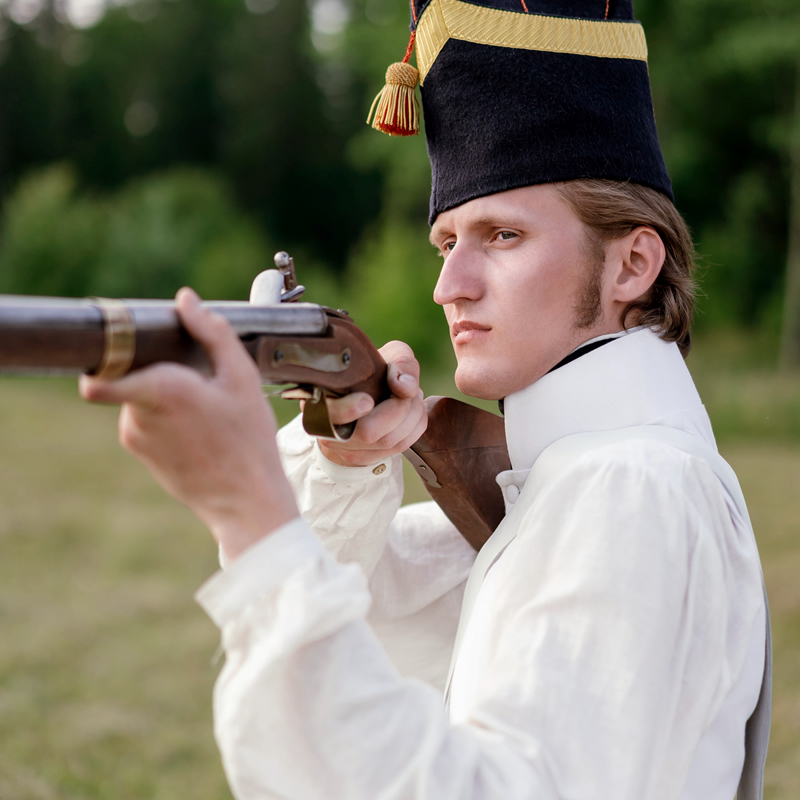 A Man in White Uniform with Black Hat Holding Rifle